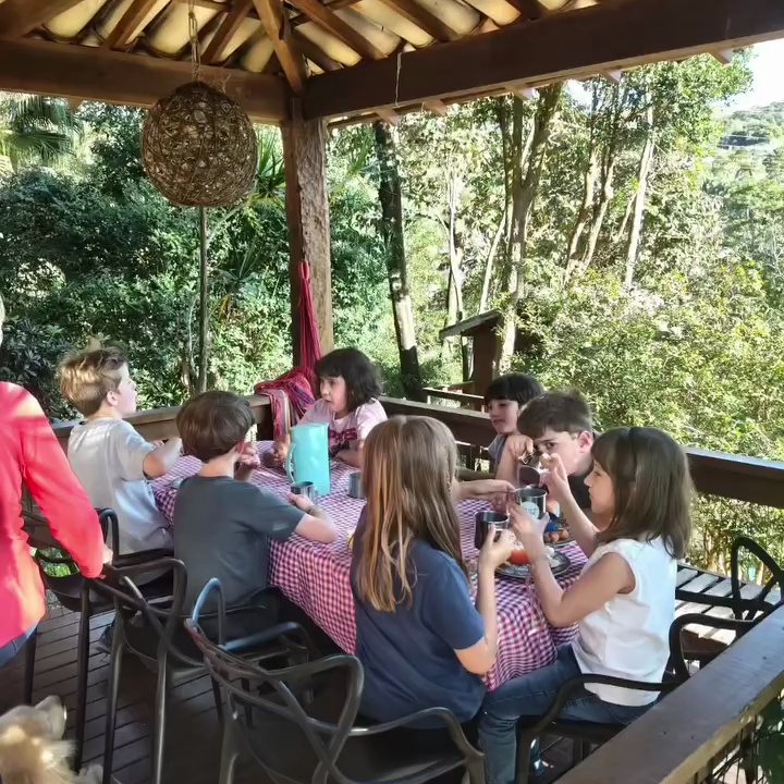 Crianças à mesa na varanda coberta, cercada de árvores